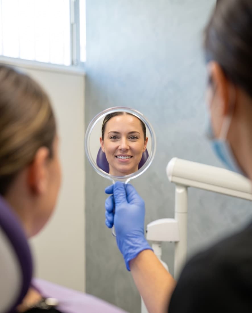 A patient seeing her restored smile in a hand mirror